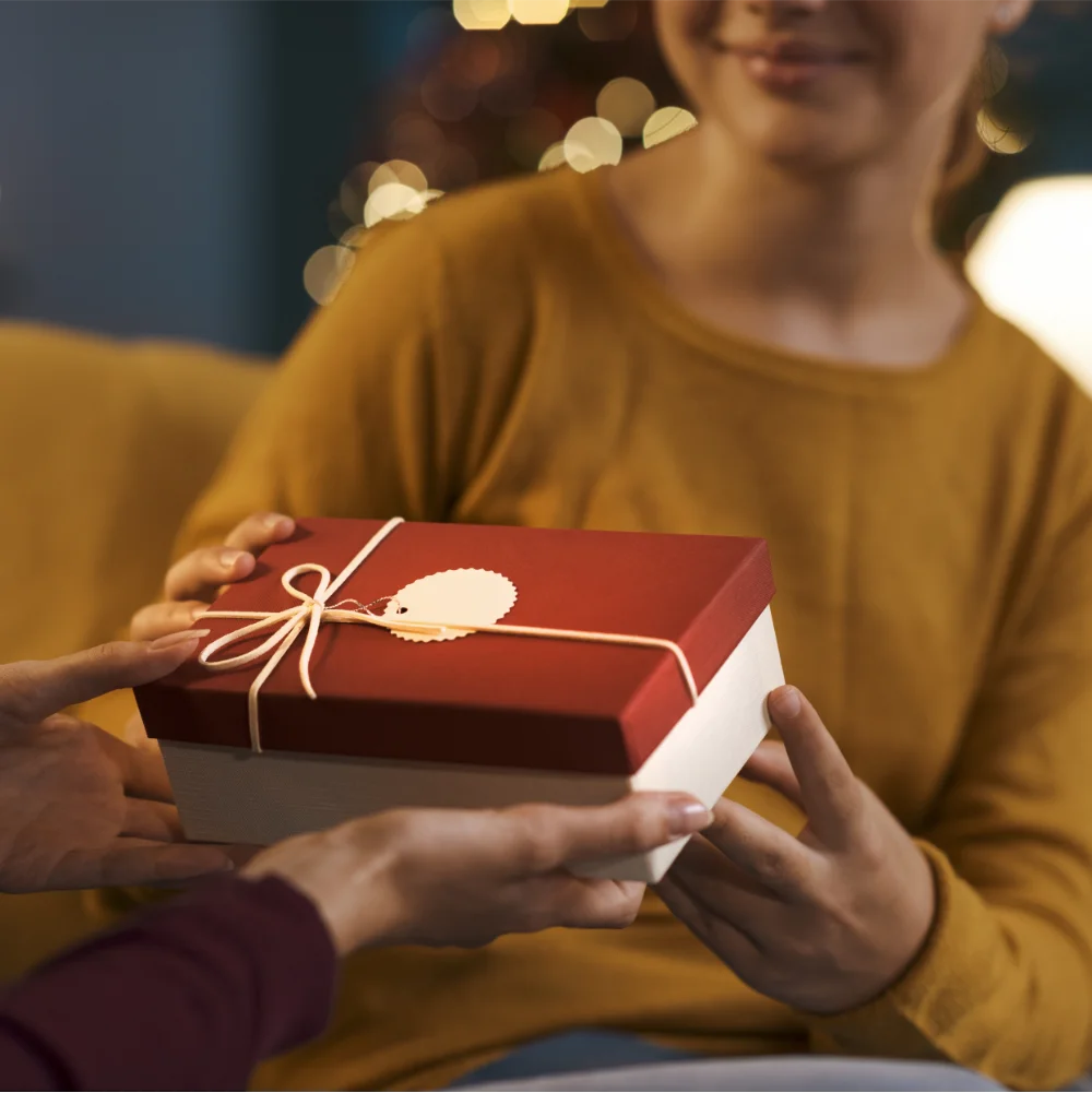 Eine Person überreicht einer anderen ein festlich verpacktes Geschenk in rot-weißer Box, Nahaufnahme der Hände